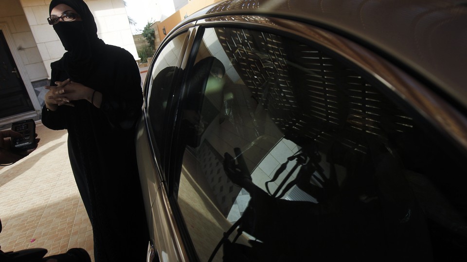 A veiled Saudi driver stands next to her car