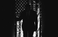 A black-and-white image of Donald Trump silhouetted in front of a draped American flag