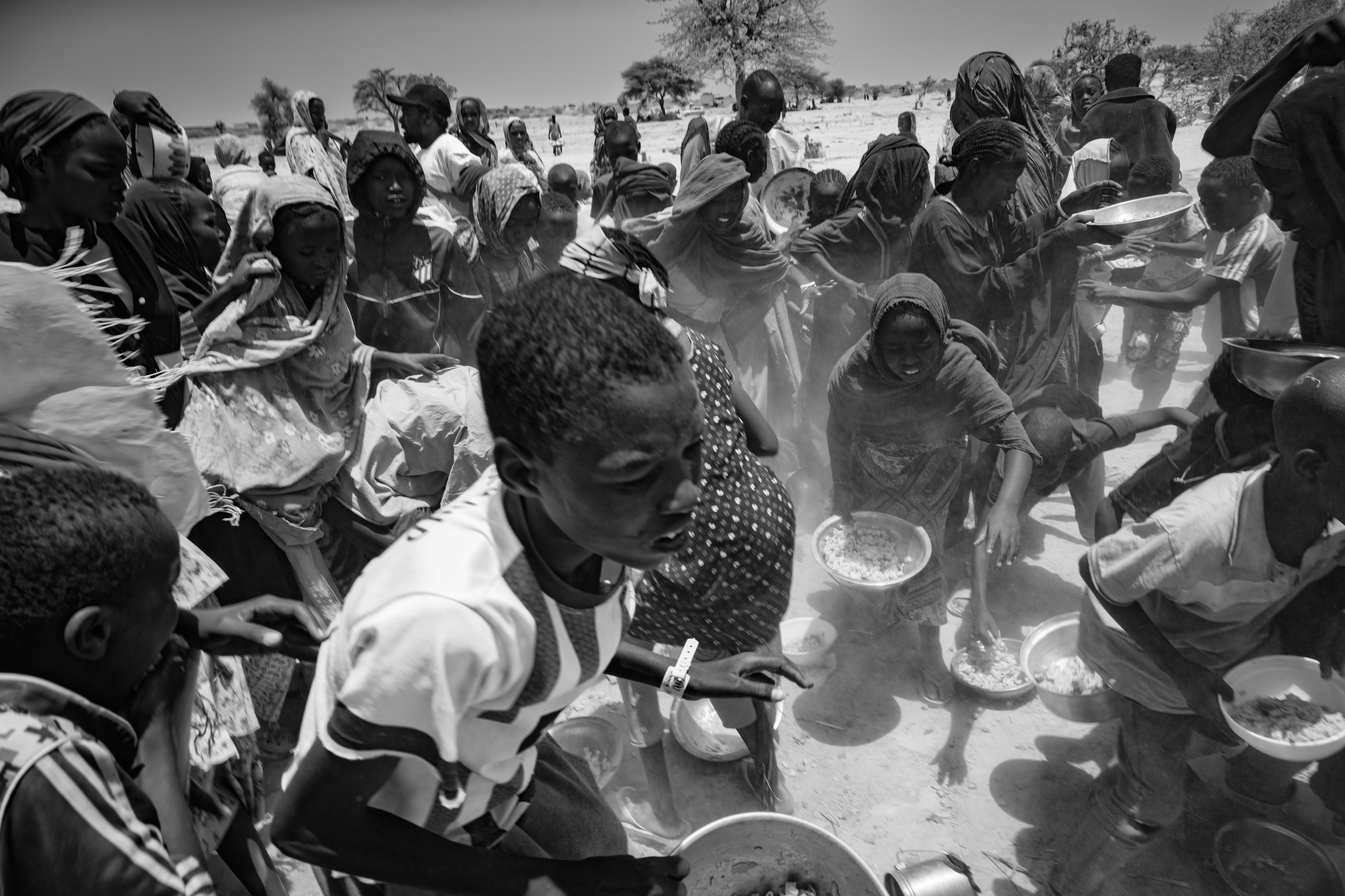 Picture of Sudanese children scrambling to grab their bowls from the ground following a food distribution by the Tiné Emergency Response Room.