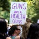 Protester holding a sign that says "Guns are a health crisis"