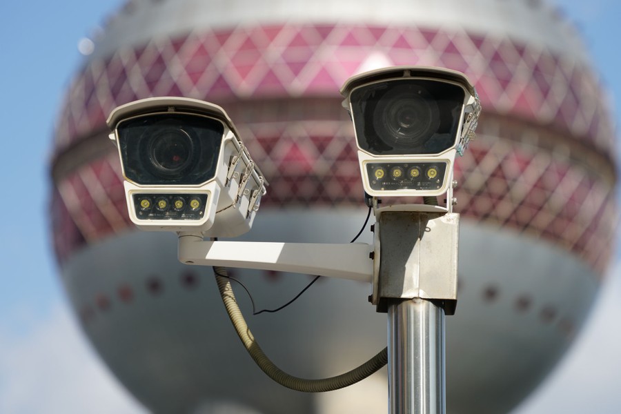 A pair of mounted security cameras, against a ball-shaped tower in the background, vaguely resembling a face