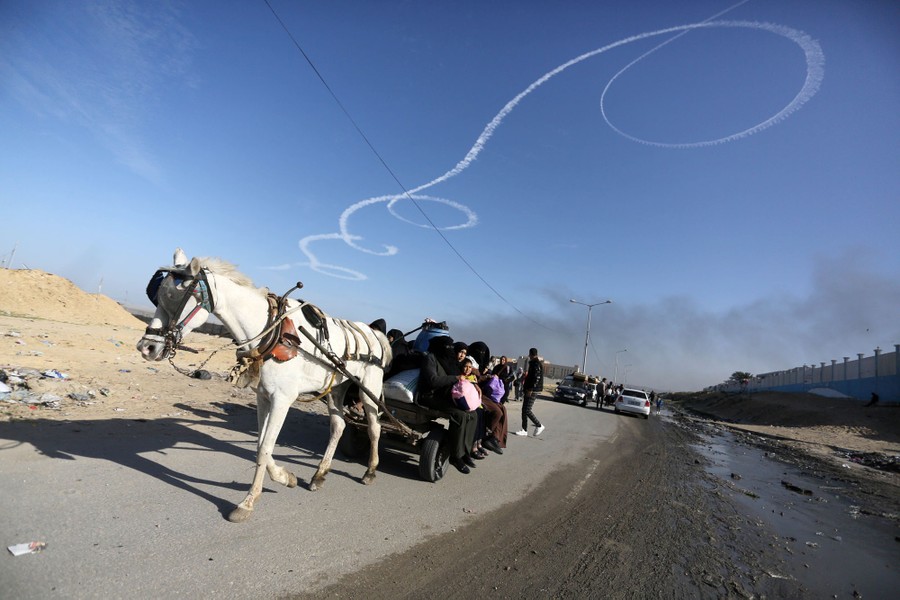 People ride down a road on a horse-drawn carriage in Gaza, beneath a spiraling jet trail in the sky above.