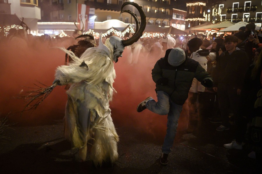 An actors dressed in a Krampus costume hits a running bystander with small sticks.