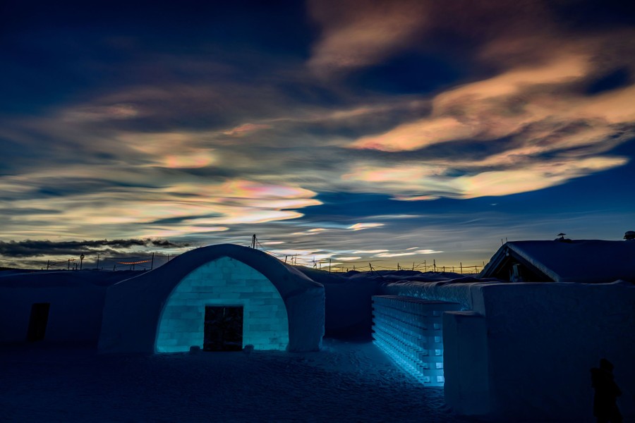 Colorful glowing clouds appear high above buildings built out of snow and blocks of ice.