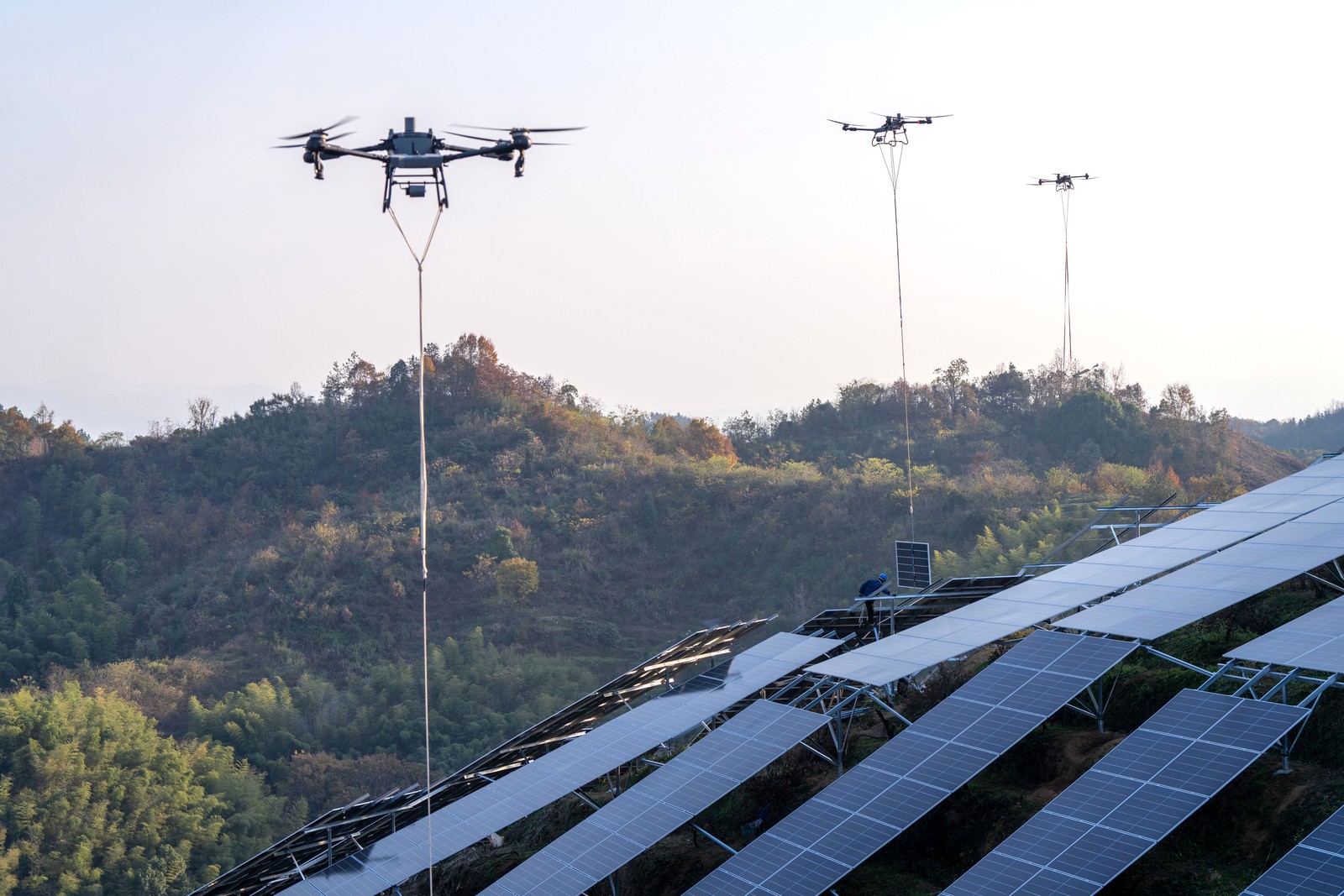 Several drones are used to lift and place solar panels along steep hillsides.