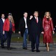 Donald Trump, Melania Trump, and the two Republican Senate candidates in Georgia walk with two others along an apparent tarmac. President Trump has his right fist raised.