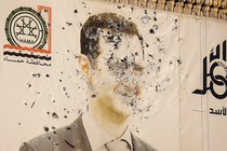 Photograph of a banner hung on a building depicting Syrian President Bashar al-Assad, riddled with bullet holes.