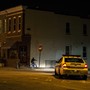 A police car sits on a street in East Baltimore, shining its headlights on a man riding a bike.