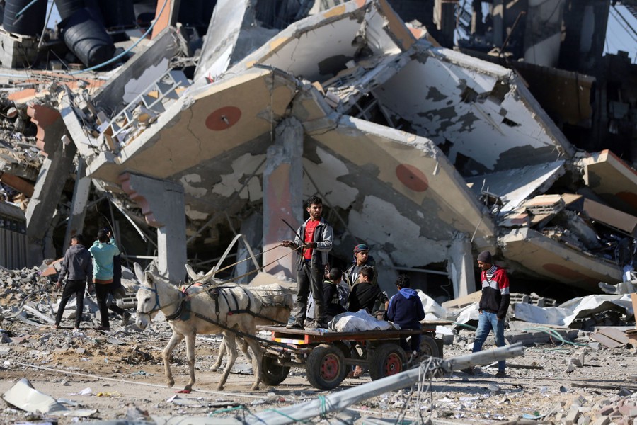 People drive a donkey cart past the ruins of a collapsed building.