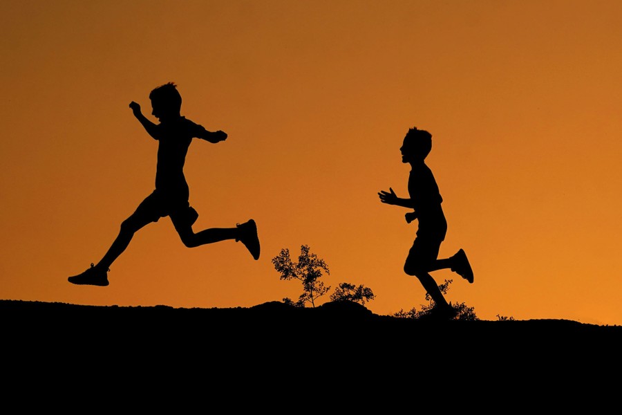 Boys, seen in silhouette, run and jump.