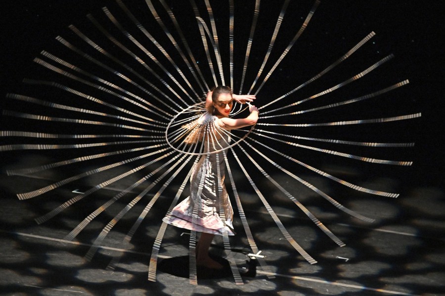A performer spins on stage, making long beaded strings fly out from their body.