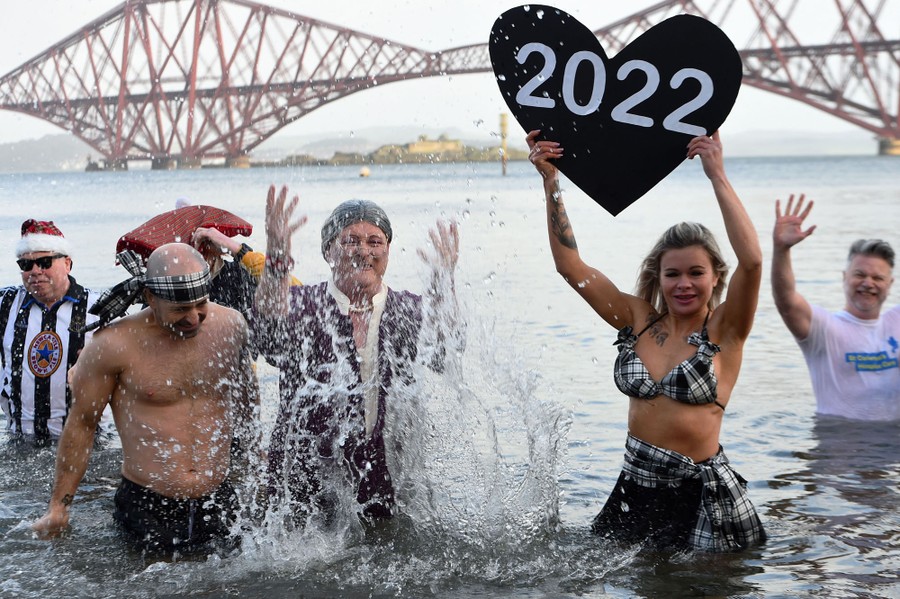 Several people stand waist-deep in water, wearing costumes. One holds up a cutout of a heart with "2022" written on it.