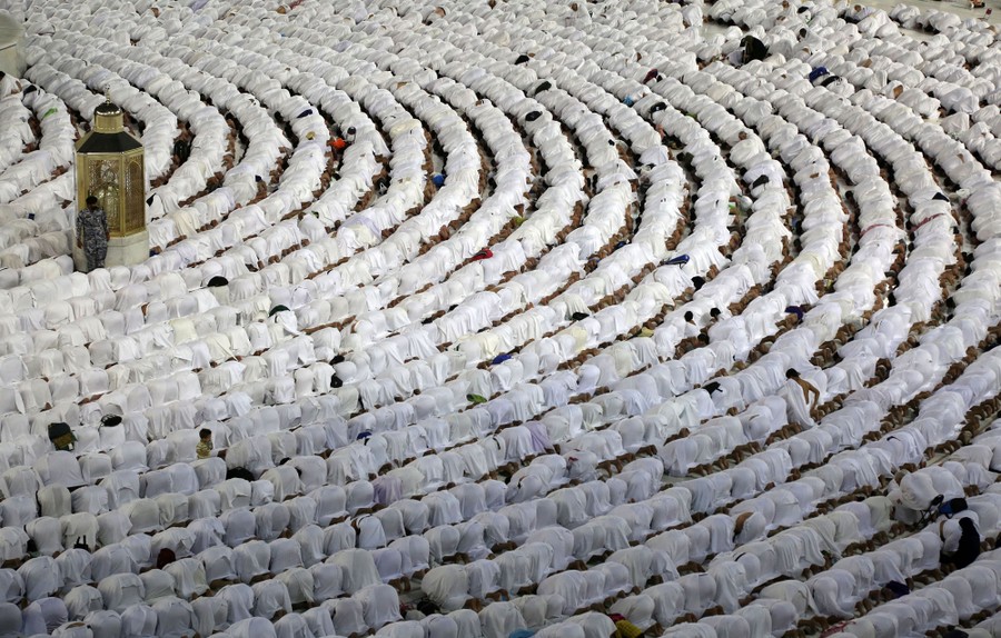 Hundreds of people in white robes kneel down in prayer in circular rows.