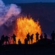 A crowd of onlookers pictured in silhouette against a fountain of erupting lava in the distance