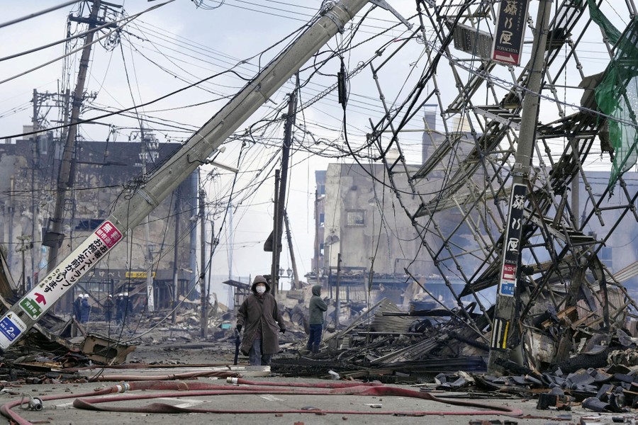 People walk past a burned-out neighborhood and huge tangles of fallen power lines.