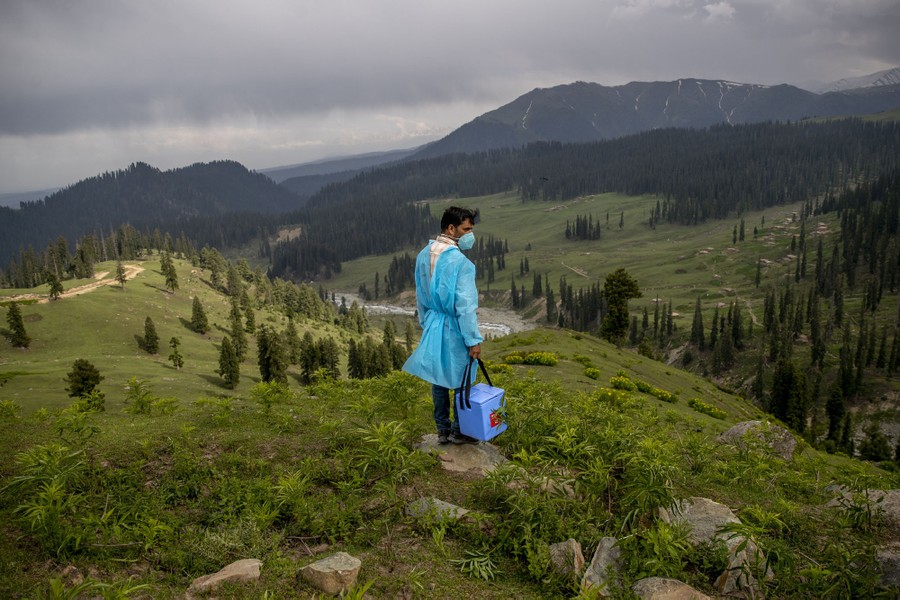 A health-care worker in protective gear stands on a hilltop in the countryside.