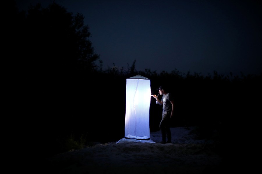 A person attends to a brightly lit device outside at night.