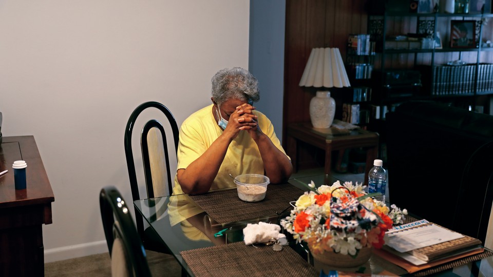 A woman sits at a table in her apartment, praying
