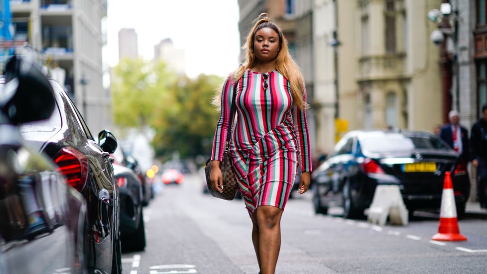 A woman in a fashionable striped dress walks down the street.