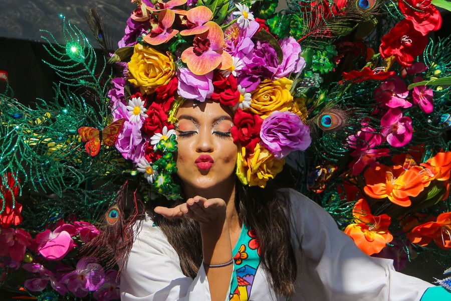 A person wearing an ornate floral headdress blows a kiss.