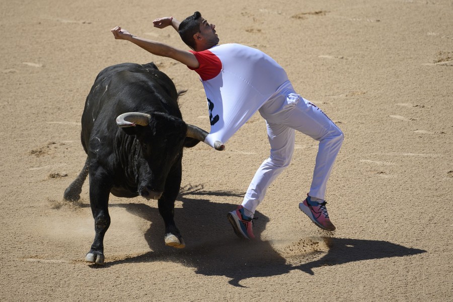 A person tries to leap away from a charging bull, but one of the bull's horns has snagged and is pulling at their shirt.
