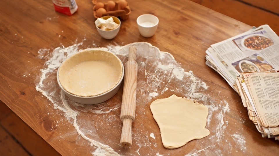 A cookbook next to a rolling pin and flattened dough 