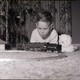 A boy looking at a toy railroad set by a Christmas tree