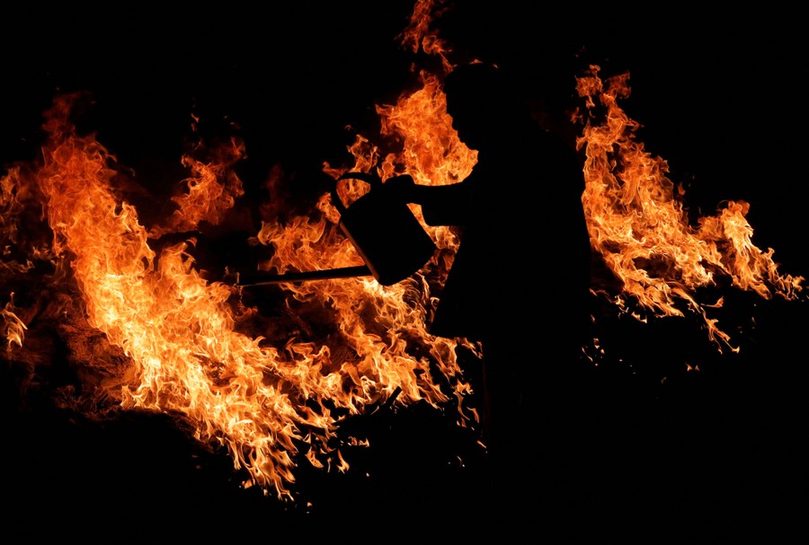 A person holding a can of gasoline is silhouetted against a large fire.
