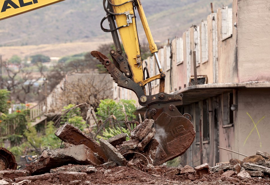 An excavator removes rubble outside of a destroyed apartment building.