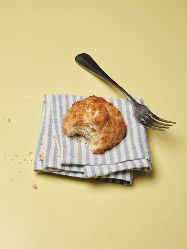 photo of biscuit with one bite taken out of it on blue-and-white-striped folded napkin with fork, on yellow background