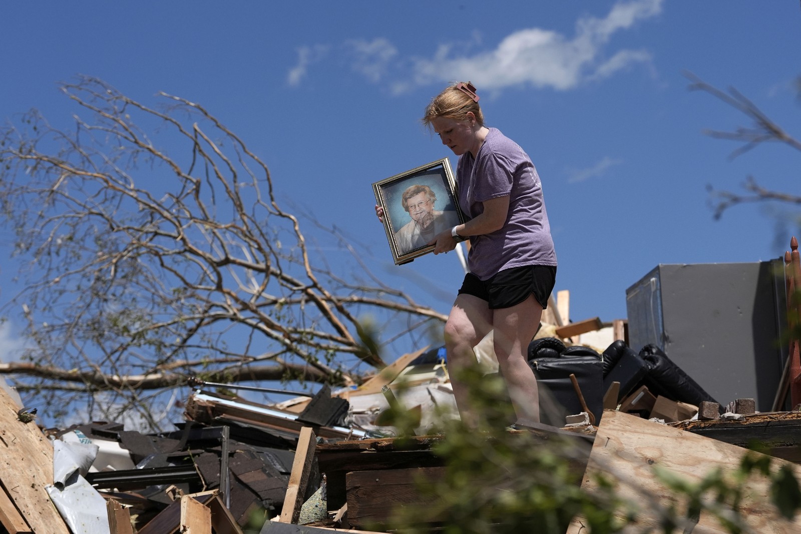 A person carries a family picture while walking over debris outside a storm-damaged house.