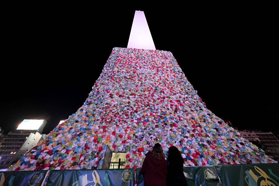 People look at a tall art installation made of plastic bags, stacked around the base of a tall obelisk.