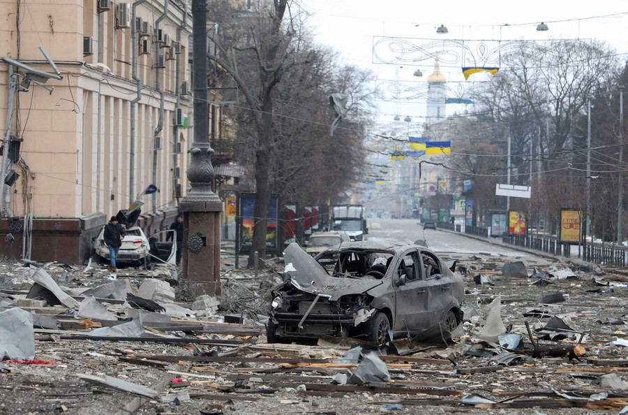 A wrecked car sits among bomb debris strewn about a city street.