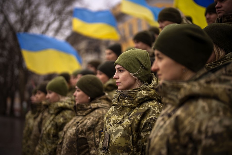 A group of soldiers pose for a group photo beside blue-and-yellow flags.