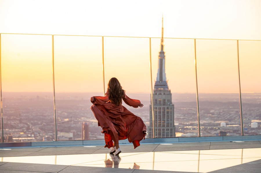 A person in a red dress looks out over a city from a high observation deck.