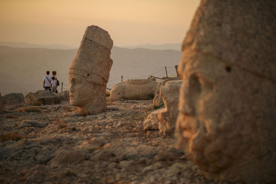 Several people walk past ancient statues on a mountaintop.