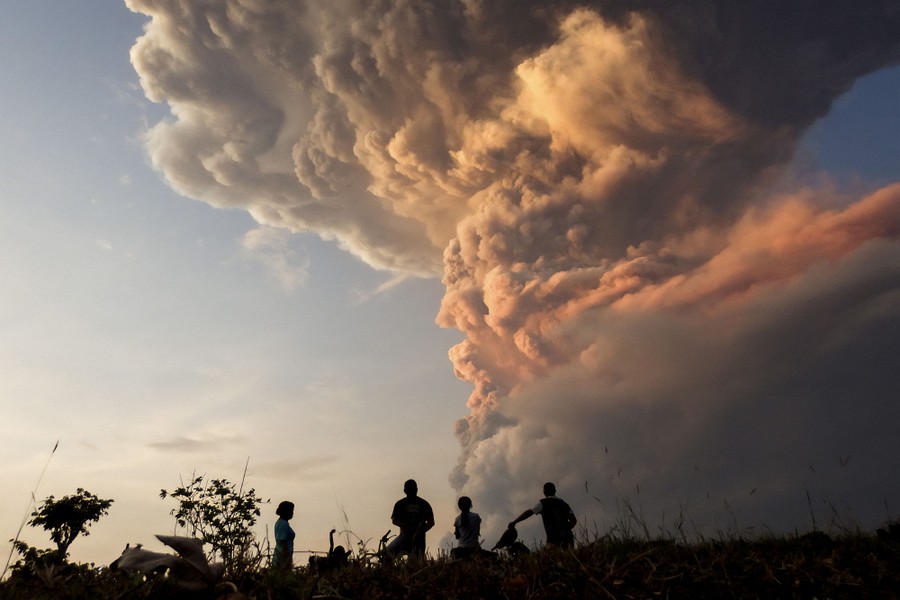 People look up toward a large column of ash rising above an erupting volcano.
