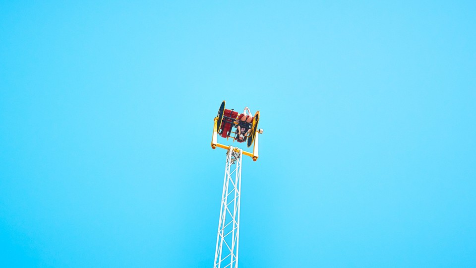 A person sits upside down on an amusement park ride, high in the air.