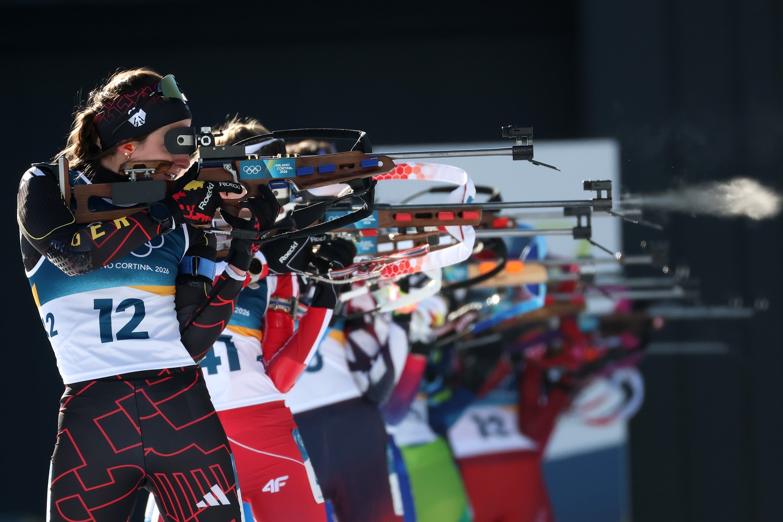 Biathletes stand side-by-side, rifles raised, during a shooting bout.
