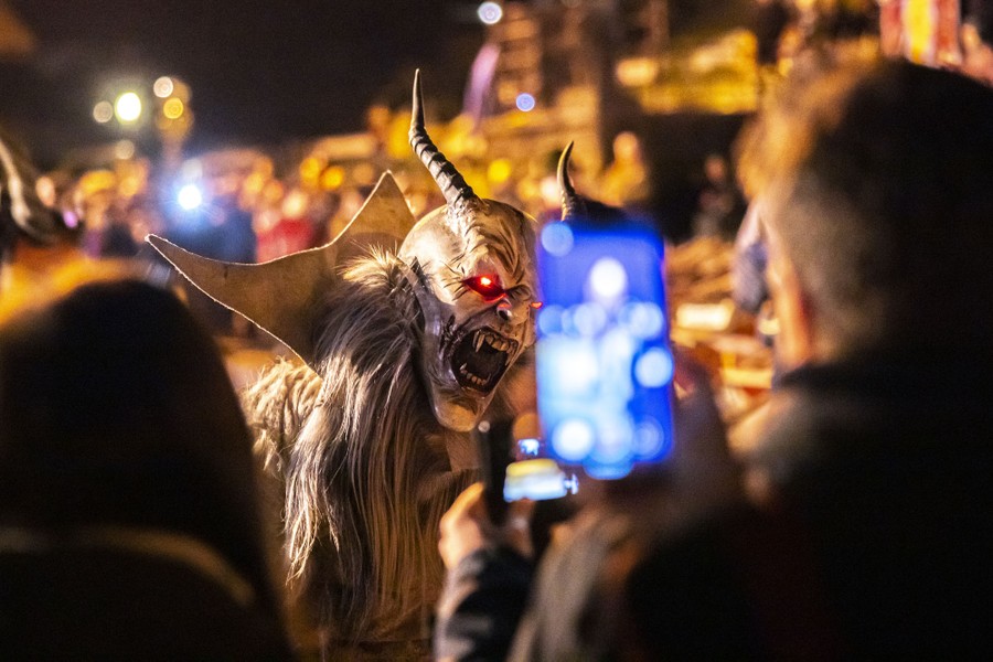 People take pictures of a performer wearing a frightening demon mask and furry costume.