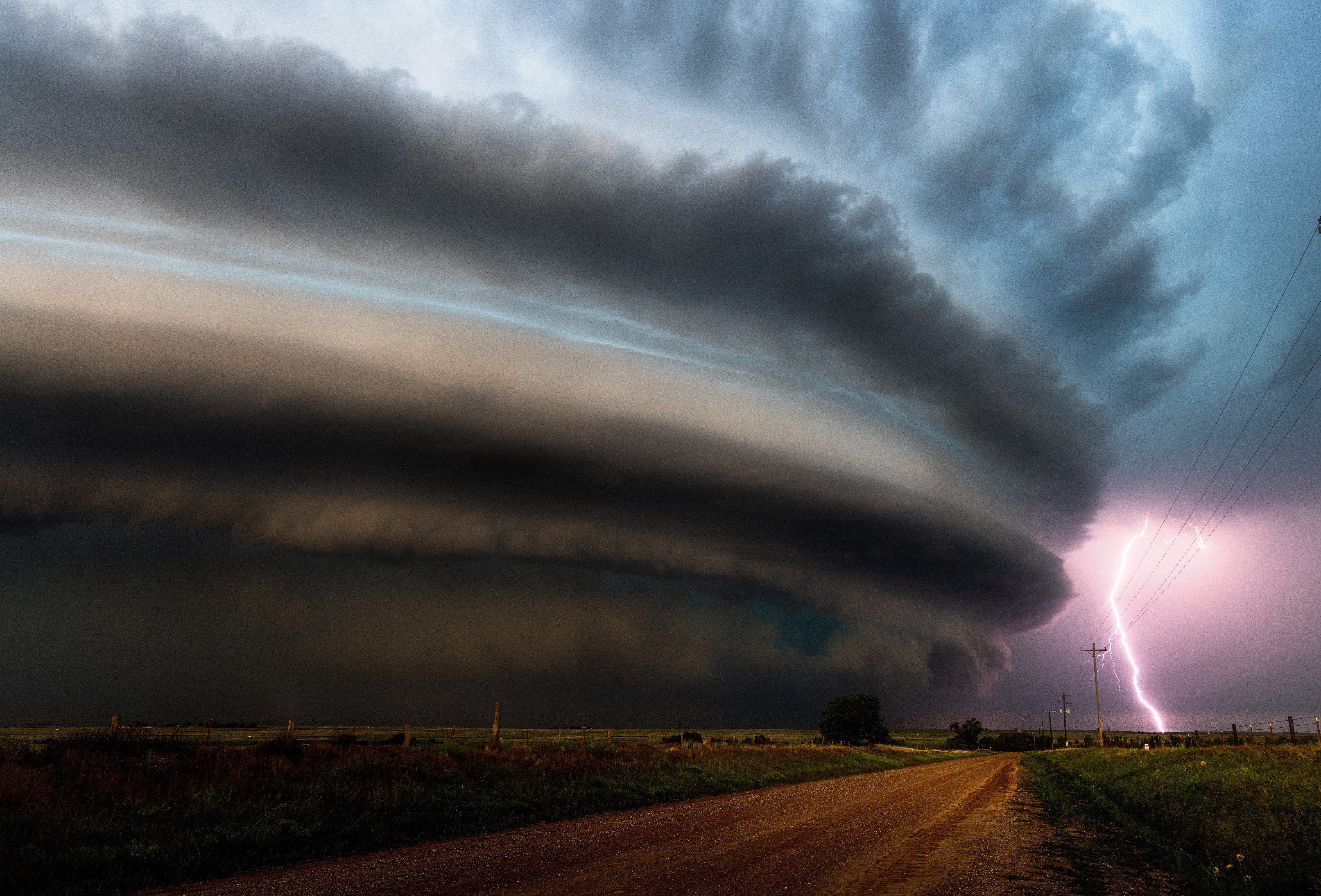 A huge, dark, cylindrical storm cloud swirls above a rural area.