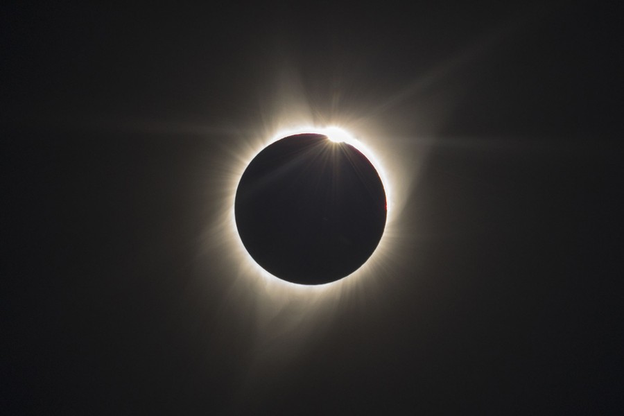 Bright rays of light appear to radiate from a dark circle, as the passing moon darkens the entire sun, leaving only the outher rays of its corona visible.
