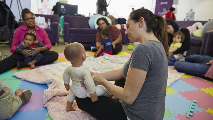One woman shows a baby doll to a circle of women and infants