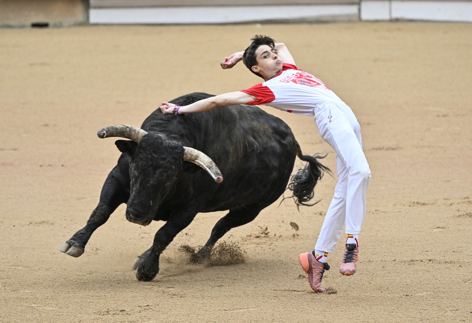 A performer leaps, avoiding a charging bull in a bullring.