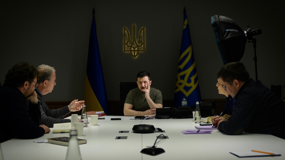 Jeffrey Goldberg and Anne Applebaum sit at a large table with President Volodymyr Zelensky and two other people.