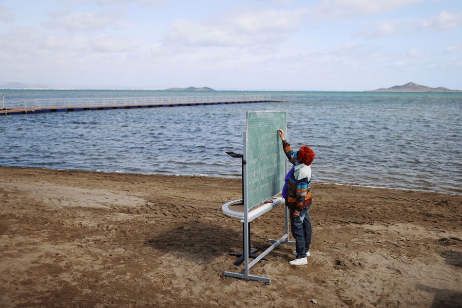 A teacher works at a blackboard set up on an empty beach.
