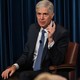 Neil Gorsuch raises his finger while speaking to an audience in front of a blue curtain