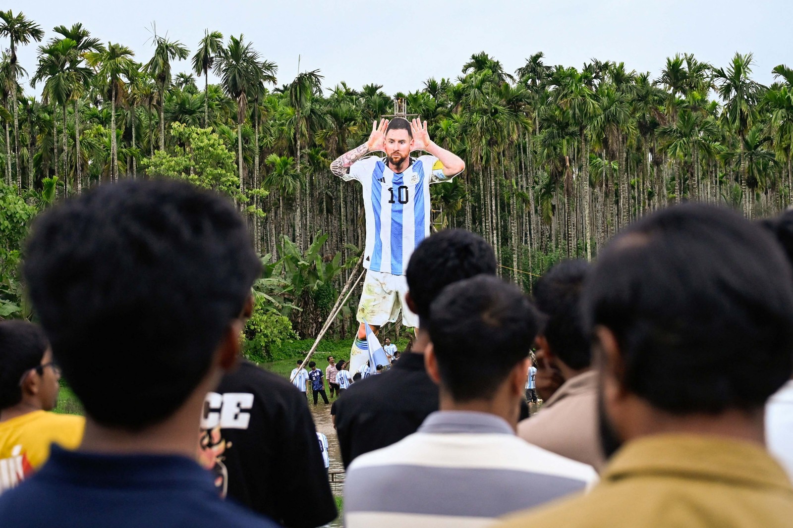 People look on as others stand up a tall cutout of Lionel Messi in a soccer uniform.