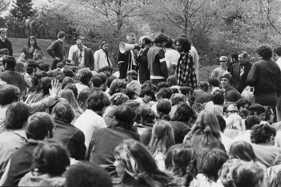 Several people stand with a bullhorn, addressing a seated crowd in front of them.