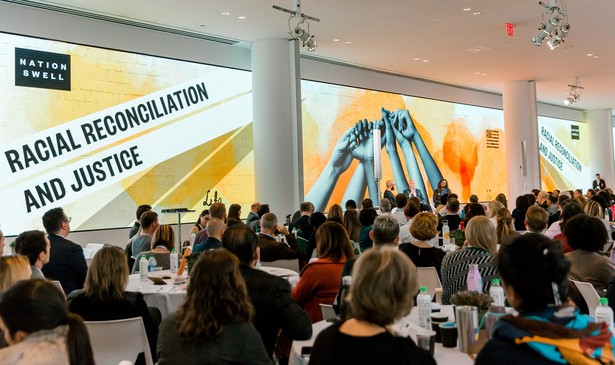People seated at tables watch speakers at a NationSwell event on